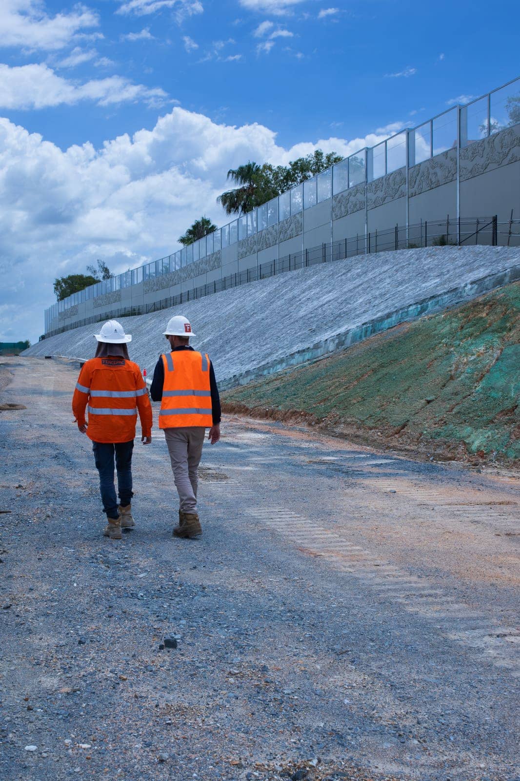 Two Fencepac staff walking beside a long retaining wall