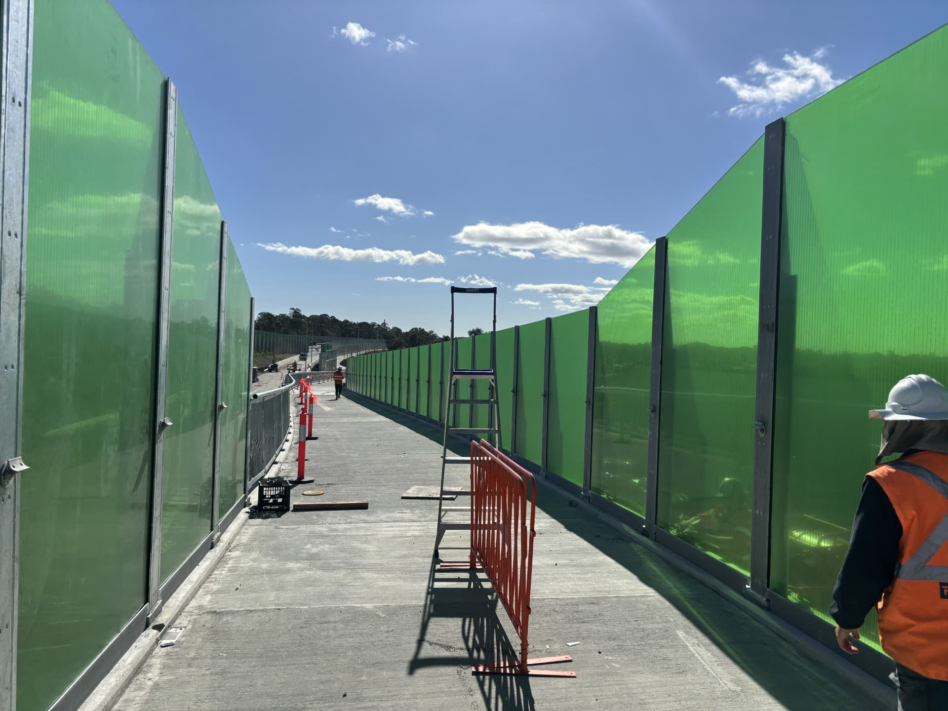 Green transparent acrylic noise wall panels along a concrete walkway