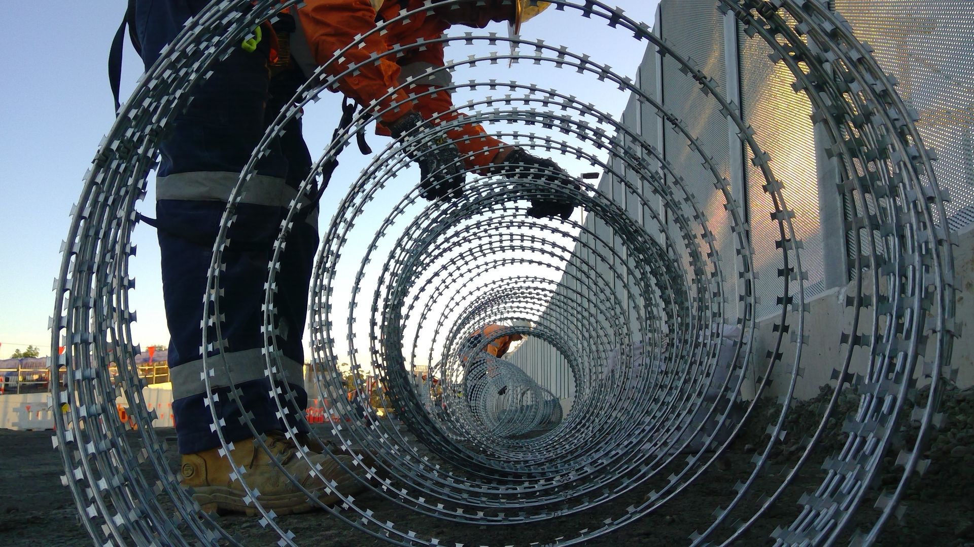 Worker with razor wire coil at security fencing installation at sunset