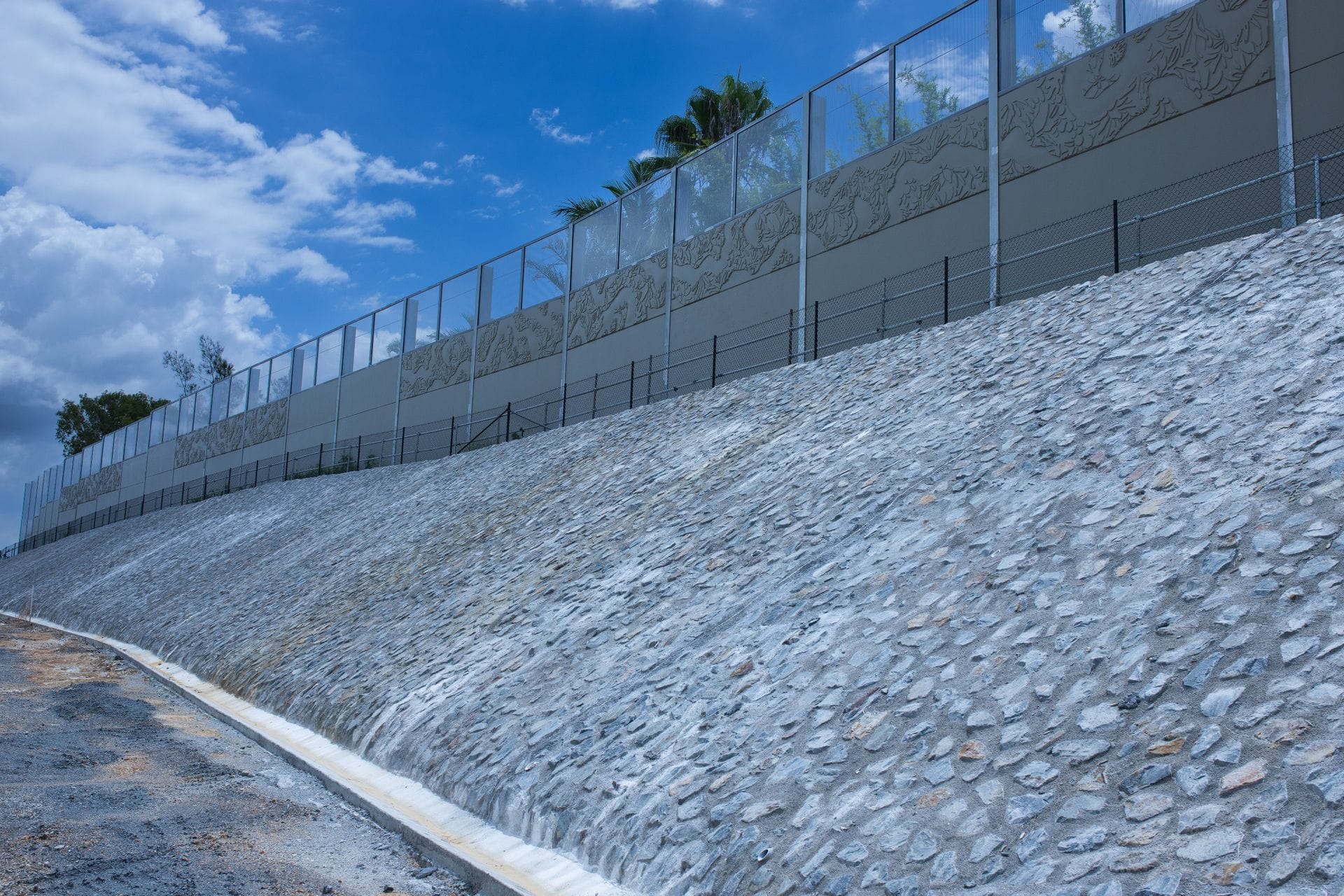 Stone pitching embankment with decorative glass-topped noise barrier above