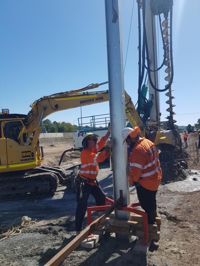 Crew installing barrier post with crane and excavator