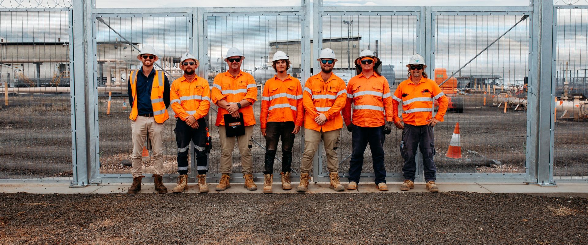 Fencepac crew of seven in hi-vis and hard hats standing in front of completed security mesh fencing